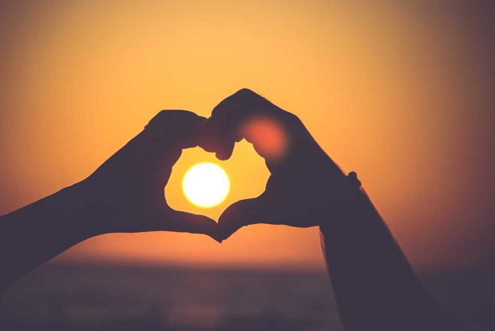 manos que forman un corazón con el sol dentro