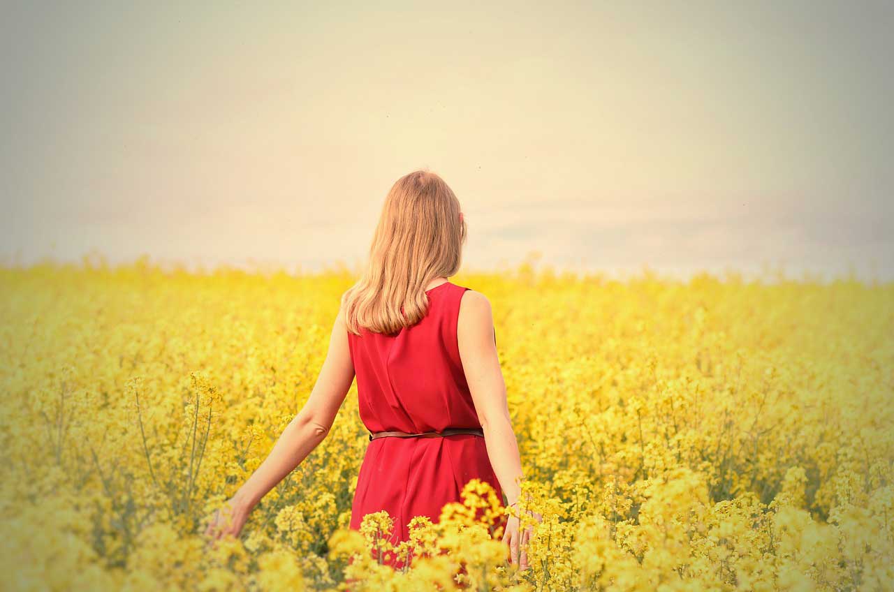 mujer de espaldas con vestido rojo en un campo de flores amarillas