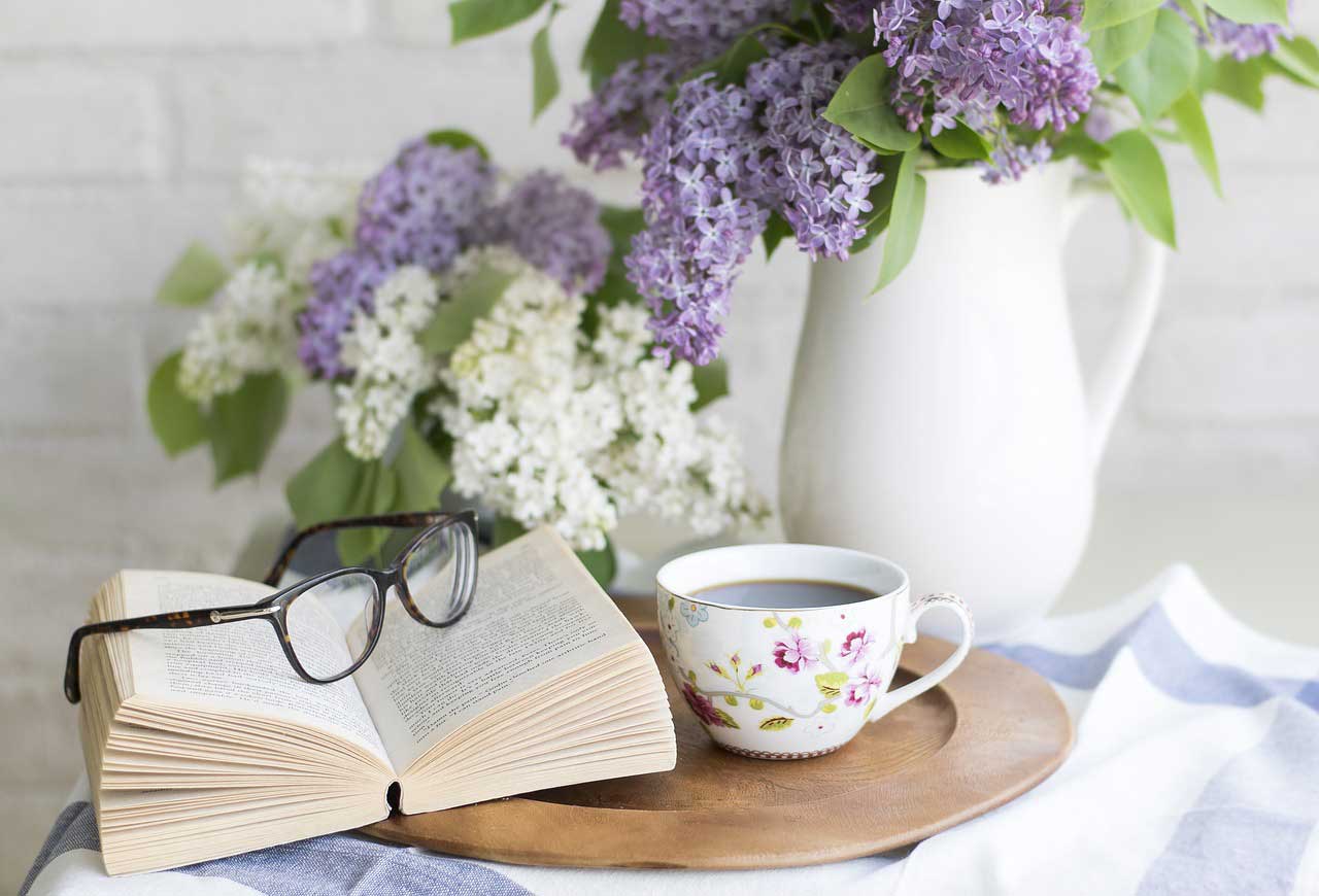 libro abierto, anteojos, taza de café y floreros con flores blanca y violetas