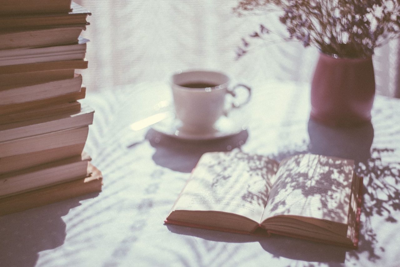 imagen romántica, libro abierto con taza de café florero y pila de libros